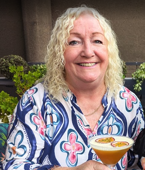 Maxine Woman with shoulder-length platinum-blonde curly hair and warm friendly smile.